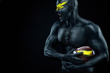 American football fan with ball on black background. Fitness and sport motivation. Strong fit and athletic guy in body paint like a super hero.の写真素材
