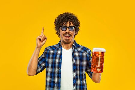 St Patrick Day. Young Oktoberfest man serving big beer mug with drink isolated on yellow background. Guy showing ok sign with fingers.の写真素材