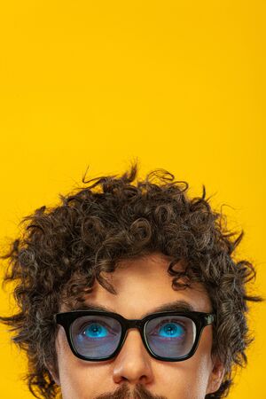 Portrait of happy bearded man with curly hair pointing finger up at copyspace isolated over yellow background. Guy in blue sunglasses pick on great idea.の写真素材