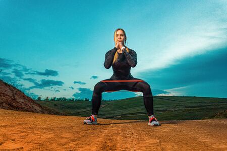 Workout with bands or expander outdoors. Individual sports recreation. Sporty and fit young woman athlete have a training on the sky background. Concept of a healthy lifestyle and sport.の写真素材