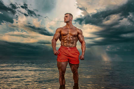 Fit athlete bodybuilder on the beach. Attractive young man lifeguard on a tropical seashore. A thunderstorm is behind the man.の写真素材