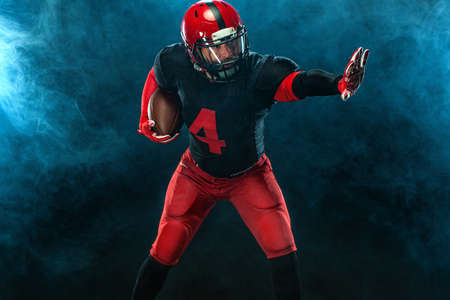 American football player, athlete sportsman in red helmet on dark background with smoke. Sport and...
