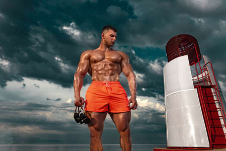 Fit athlete bodybuilder with binoculars in hand on the beach . Attractive young man lifeguard near the observation tower.の写真素材