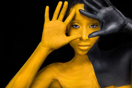 Face art. Woman with black and yellow body paint. Young african girl with colorful bodypaint. An amazing model with yellow makeup. Closeup face.の写真素材