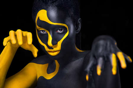 Face art. Woman with black and yellow body paint. Young african girl with colorful bodypaint. An amazing model with yellow makeup. Closeup face.の写真素材