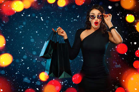 Black Friday sale concept for shop. Shopping woman in sunglasses holding red bag isolated on dark...