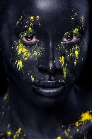 Woman with black body paint. Cheerful young african girl with art bodypaint. An amazing model with yellow makeup. Closeup face.の写真素材