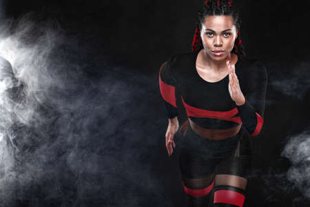 Strong athletic woman sprinter, running on black background wearing in the sportswear. Fitness and...