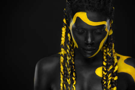 Yellow and black body paint. Woman with face art. Young girl with colorful bodypaint. An amazing afro american model with makeup.の写真素材