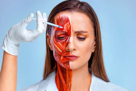 Cosmetic injection in the face. Young woman with half of face with muscles structure under skin. Model for medical training on a light background. Close up photo of face human anantomy.の写真素材