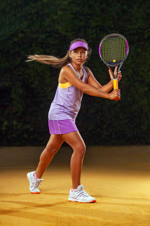 Tennis player kid. Beautiful girl teenager and athlete with racket in pink sporswear and hat on tennis court. Fashion and sport concept.の写真素材