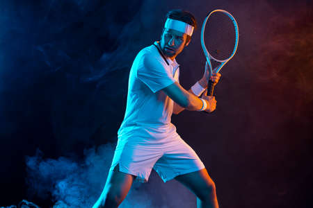Tennis player with racket in white t-shirt. Man athlete playing on dark background.の写真素材
