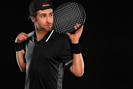Tennis player with racket in black t-shirt. Man athlete playing isolated on dark background.の写真素材