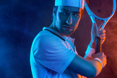 Tennis player with racket in white t-shirt. Man athlete playing on dark background.の写真素材