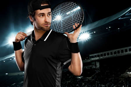 Tennis player with racket in black t-shirt. Man athlete playing on grand arena with tennis courts.の写真素材