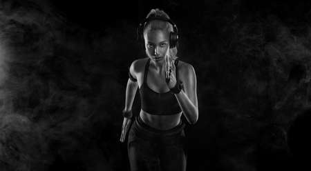 Sprinter run. Strong athletic woman running on black background wearing in the sportswear. Fitness and sport motivation. Runner concept.の写真素材