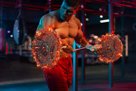 Bodybuilding in the fire. Muscular bodybuilder athlete pumping up muscles with barbell in gym.の写真素材