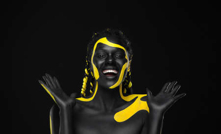 Woman on poster with gold face art. Yellow and black colors of body paint. Young girl with bodypaint. An amazing afro american model with makeup.の写真素材