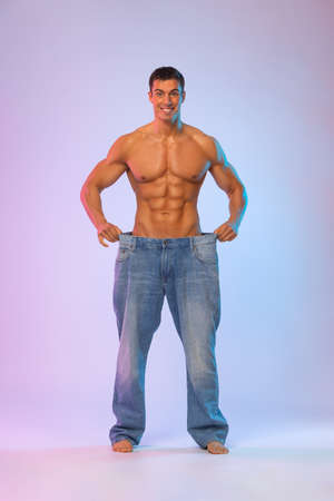 Young man showing how much weight he lost with big jeans. Fat to fit concept. Fitness posterの写真素材