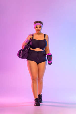 Go to the gym. Size plus model woman with bag in sportswear on pink background. Sports and healthy...