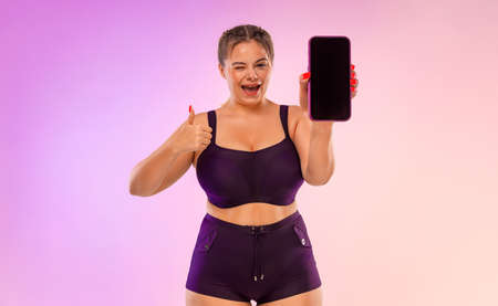 Girl Showing Thumb To App On Mobile phone. Woman Showing Smartphone Screen On Purple Studio Background. Smiling Girl on Ads Template.の写真素材