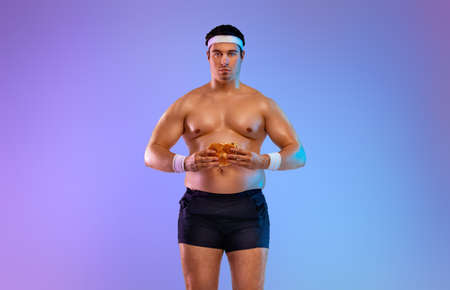 Fat man with fast food. Not sporty men drinking and eating hamburger isolated on purple background.の写真素材
