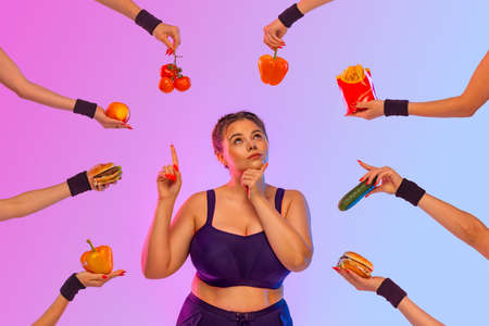 Fat girl, Plus size model girl in front of a difficult food choice. What to choose vegetables, fruits, meat, or fast food. Idea for a social media post about diet and weight lossの写真素材