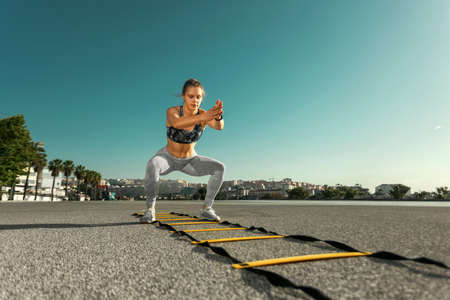 Young sportswoman training jumping on an agility ladder coordinating outdoorsの写真素材