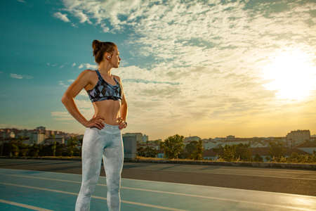 Sporty woman with fit body in sportswear posing on running track at sunrise.の写真素材