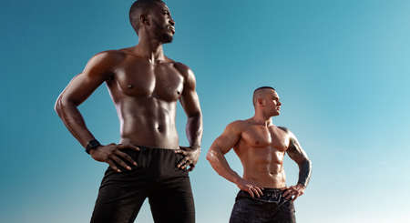 Two fit men, athletes standing on the blue sky background on start before run. Healthy lifestyle and sport. Fitness concept.の写真素材