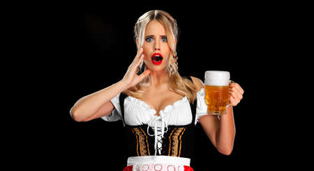 Oktoberfest 2022 in Munich. Sexy Oktoberfest girl waitress, wearing a traditional Bavarian or german dirndl, serving big beer mugs with drink isolated on black background.の写真素材