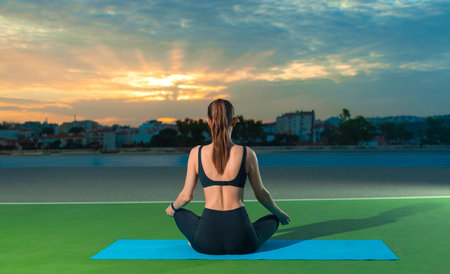 Woman practicing yoga outdoor. Beautiful girl practice asana in online class. Calmness and relax. Background with sunsetの写真素材