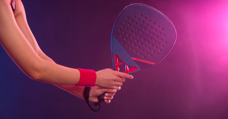 Close-up photo of Padel tennis player with racket on tournament. Girl athlete with paddle racket on court with neon colors. Download a high quality photo for design of a sports app or tour events.の写真素材