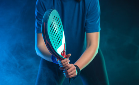 Close-up photo of padel tennis player with racket on tournament. Girl athlete with paddle racket on court with neon colors. Sport concept. No face.の写真素材