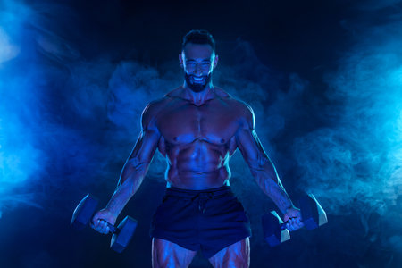 Sporty fit man athlete with dumbbells make fitness exercises on blue neon background. Download cover for music collection for fitness classes. Sports recreation.の写真素材