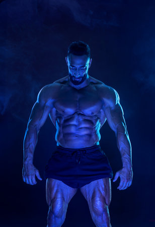 Athlete bodybuilder in blue neon colors. Fit man posing on black background. Sports concept....
