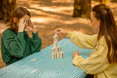 Domino game. Happy family playing board games outdoors in the park. Mom and teen girl playing...