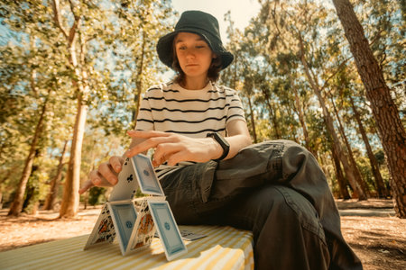 Smiling teenager girl playing card game with family. Creative outdoors leisure and education of kid. Family activity at the park.の写真素材