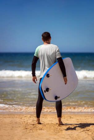 Surfer man learning to surf on foam in the ocean. First surfing lesson. Amateur surfer. Surfing training. Photo for surfing school advertising on social media.の写真素材