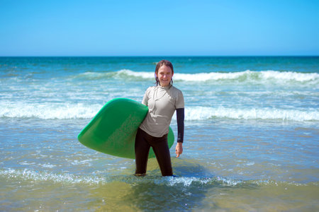 Teenage girl learning to surf on foam in the ocean. First surfing lesson. Amateur surfer. Surfing training. Photo for surfing school advertising on social media.の写真素材