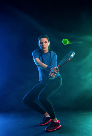 Padel tennis player with racket on tournament. Girl athlete with paddle racket on court with blue neon colors. Sport concept. Download a high quality photo for design of a sports app or tour events.の写真素材