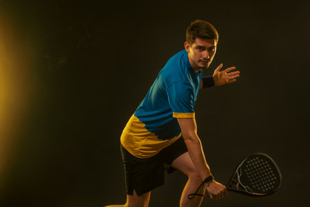 Padel Player with Racket in Hand. Paddle Tennis, on a black background with yellow lights.