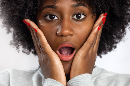 Confident smiling woman in pink top on light background. Black female portrait with an emotion of surpriseの写真素材