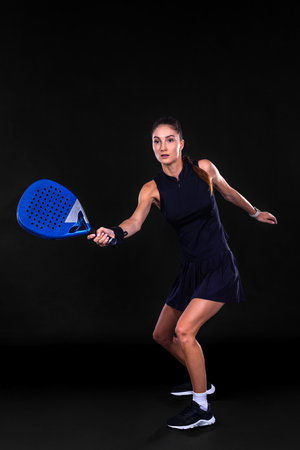 Young female athlete playing padel in dark neon studio light showing powerful movement energy and sport focus during gameの写真素材