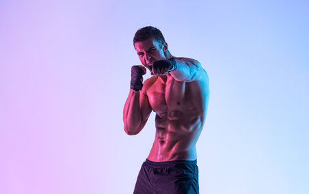 Male boxer in hand wraps practicing punches on purple neon background during intense workout showing strength speed and focus in dramatic studio lighting fitness and martial arts conceptの写真素材