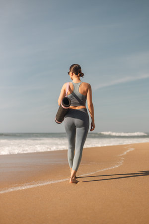 Woman in sportswear with yoga mat by the shore promotes balance fitness and healthy lifestyle by the ocean.の写真素材
