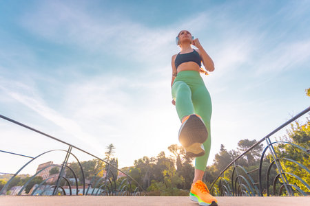 Young fit woman running outdoors in headphones during sunrise. Active female enjoying morning cardio workout for health and energy in nature. Sport lifestyle and fitness motivation concept.の写真素材