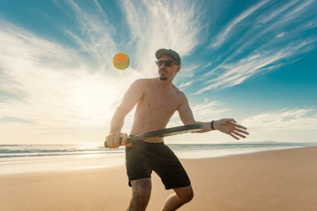 Beach tennis player hitting the ball on sandy shore during sunset training with dramatic sky and ocean waves in backgroundの写真素材