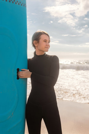 Surfer. Teenage girl resting with the surf board near the ocean. First surfing lesson. Amateur surfer. Surfing training. Photo for surfing school advertising on social media.の写真素材
