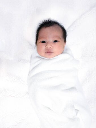 Portrait of lovely baby girl on fleece blanket, swaddled white cloth, 2 weeks oldの写真素材
